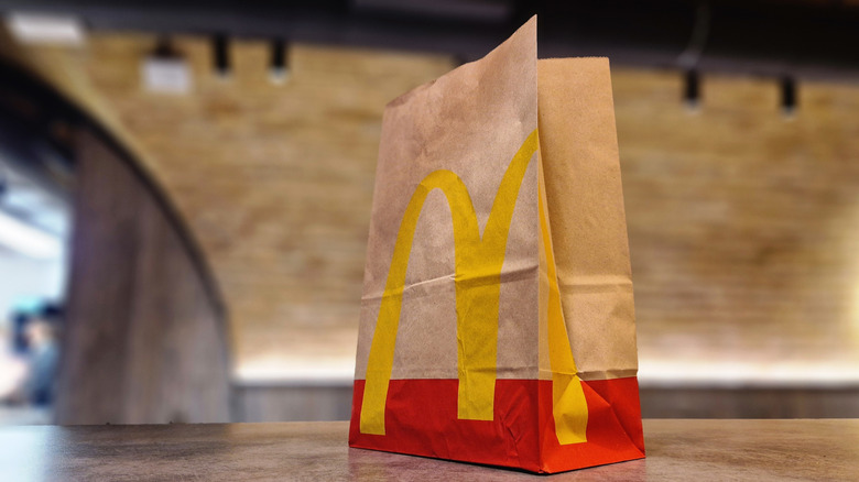 Paper bag with McDonald's logo on table, blurred interior background.