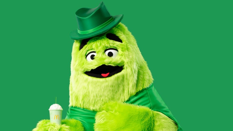 Uncle O'Grimacey character holding Shamrock Shake against green background.