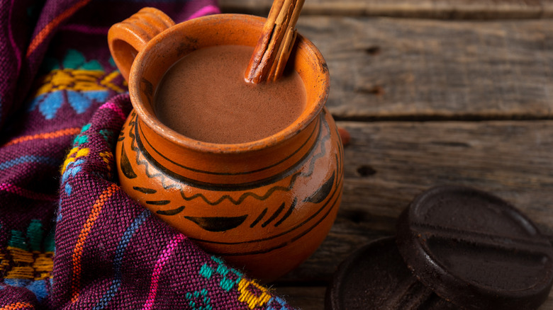 A mug of Mexican hot chocolate sits against a rustic background