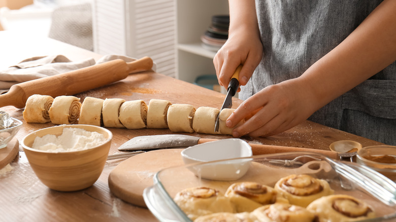 A person slicing cinnamon roll dough