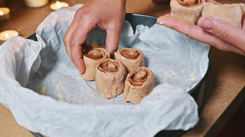 A person putting cinnamon rolls in a pan before baking