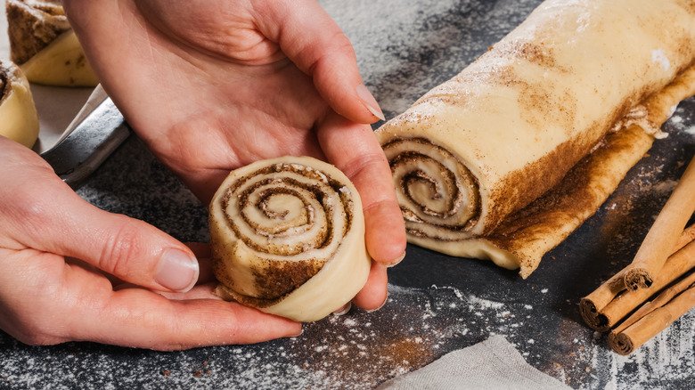 A person holding a rolled-up cinnamon roll