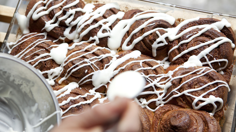 A person drizzling icing on cinnamon rolls