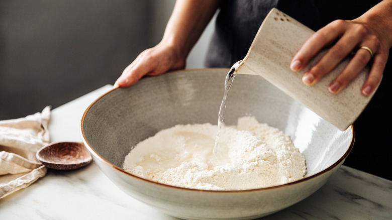 A person pouring water into a bowl of flour