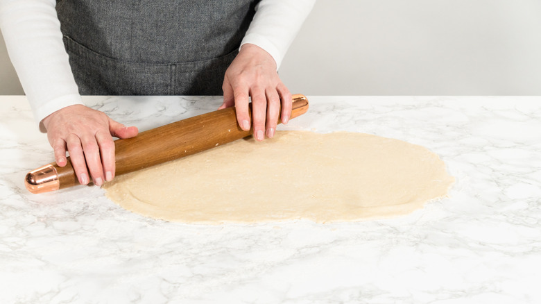 A person rolling out cinnamon roll dough on the counter