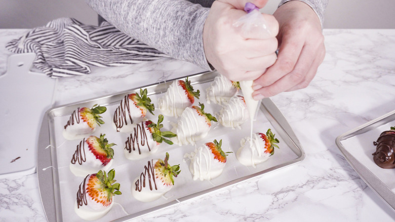 Drizzling melted white chocolate on chocolate-covered strawberries