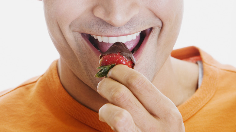 A person eating a chocolate-covered strawberry