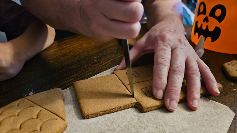 A person cutting a gingerbread cookie with a knife