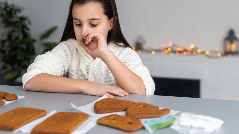 A girl looking at gingerbread house pieces