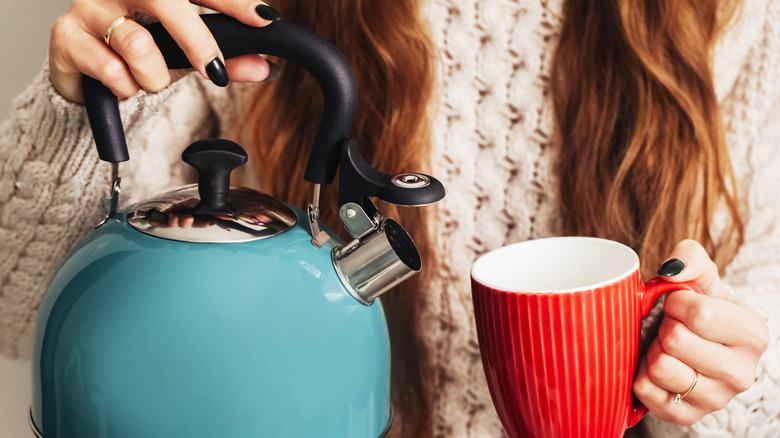 A person holding a mug and a kettle of boiling water