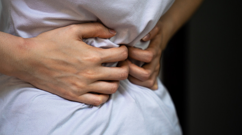 Close-up of someone in a white T-shirt clutching their stomach