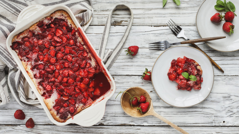 A baking dish full of sonker or cobbler, and a plate with a serving of it along with strawberries on a small plate.