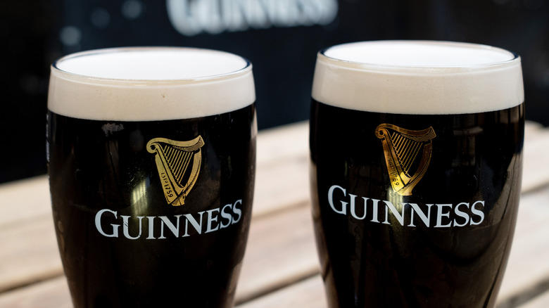 Two foamy pints of Guinness stout sit on a tabletop.