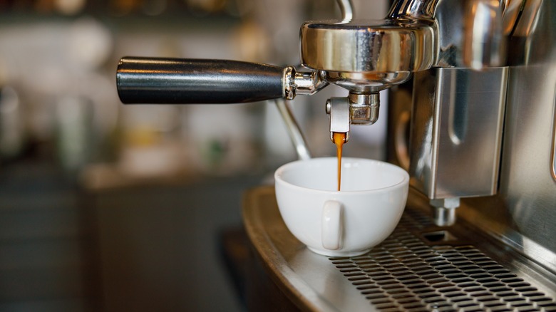 Espresso dispensing from a machine into small white cup.