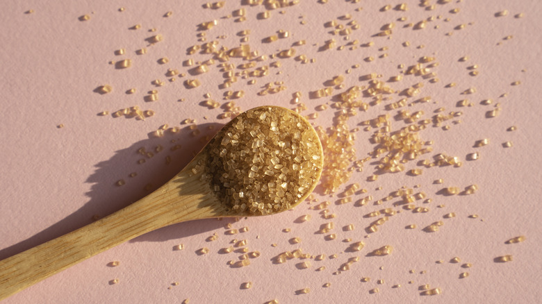 Granules of brown sugar on a wooden spoon.