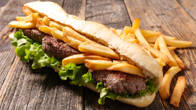 Steak sandwich with french fries inside on wood table