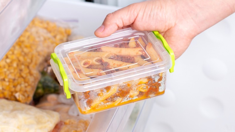 Person pulling pasta dish in plastic container from freezer