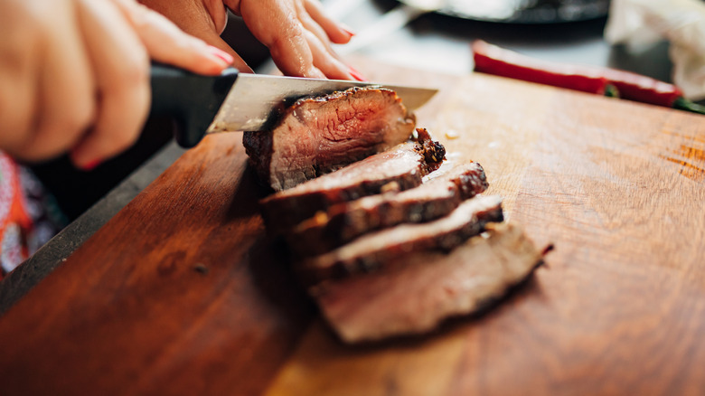 Slicing steak with a knife on a kitchen cutting board