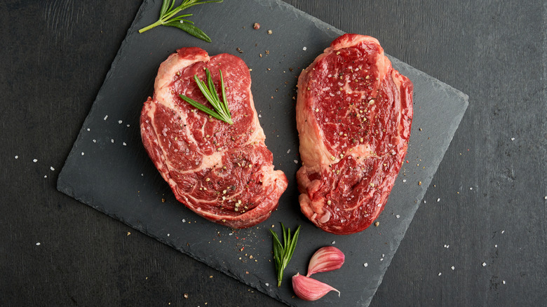 raw ribeye steaks on black stone with herbs