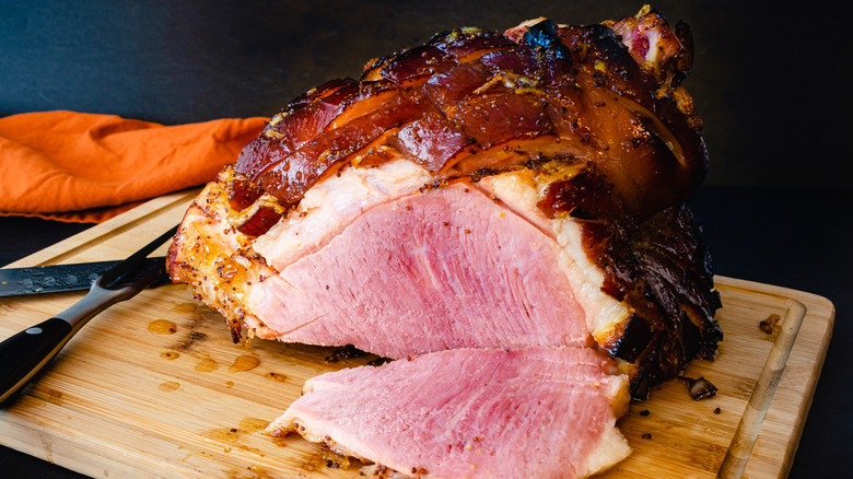 A scored ham sits atop a carving board