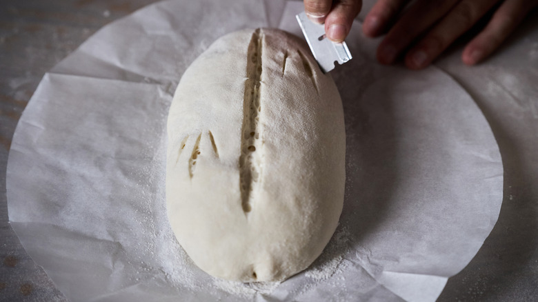 Unbaked loaf being scored with a razor blade.