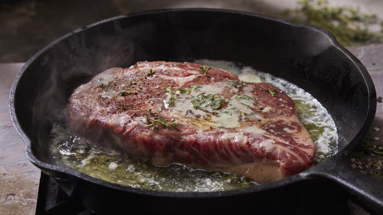 A large steak cooking in a cast iron