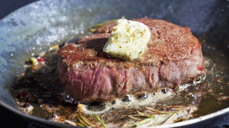 Steak in a pan topped with butter and seasonings