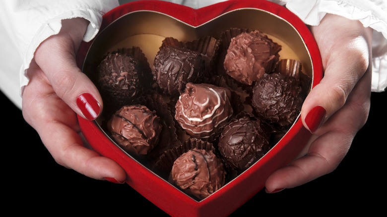 A woman's hands hold a heart-shaped box of chocolate truffles