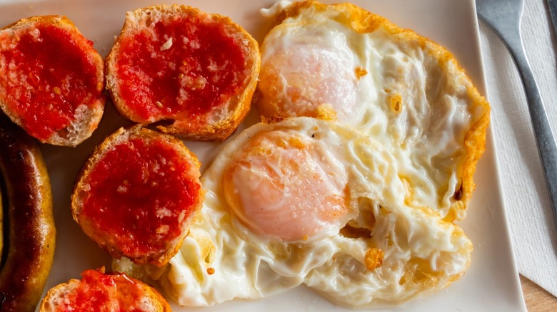 Spanish-style fried eggs with sausage and tomato bread on white plate