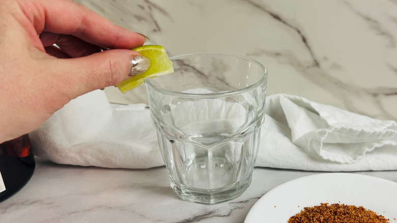 Hand rubbing lime wedge on glass