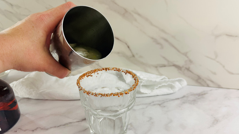 Hand pouring cocktail shaker over prepared margarita glass