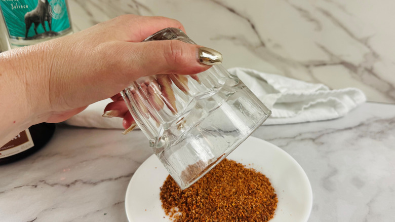 Hand rubbing rim of glass in Tajín on plate