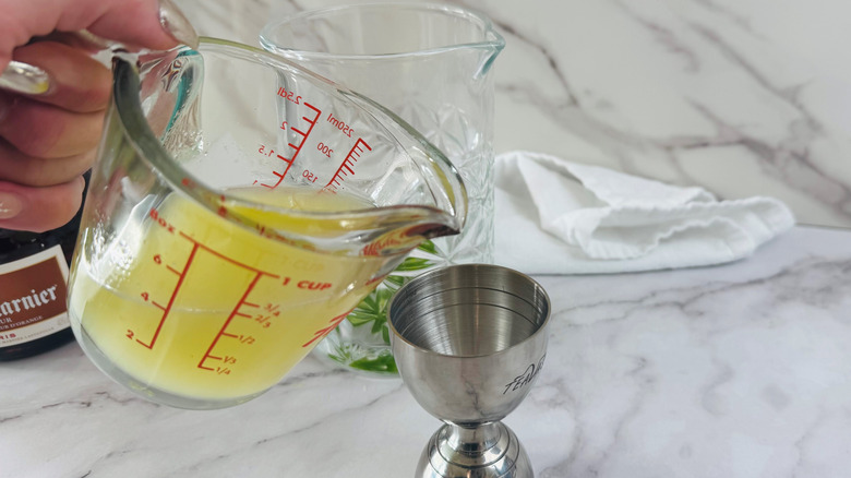 Measuring cup full of lime juice pouring into jigger