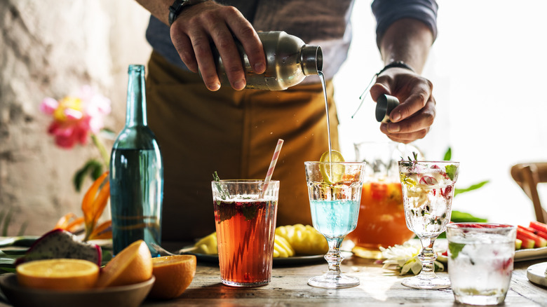 Person pouring light blue liquid from a cocktail shaker into a clear glass