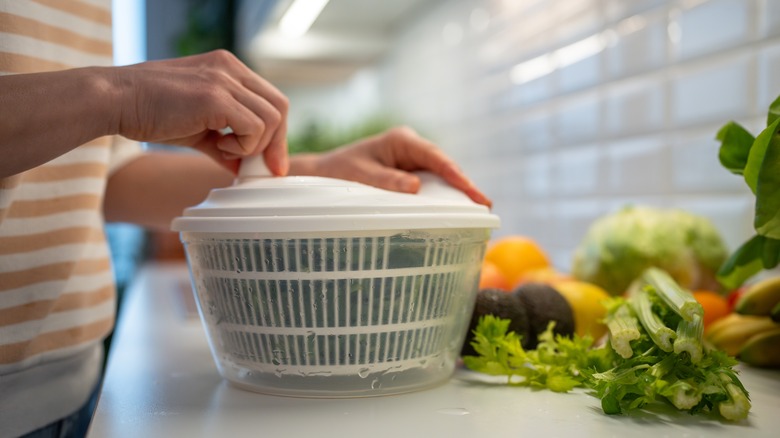 Person using salad spinner with produce nearby