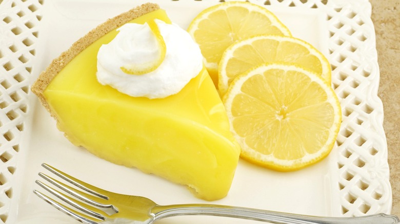 Lemon pie with lemon slices and fork on white plate