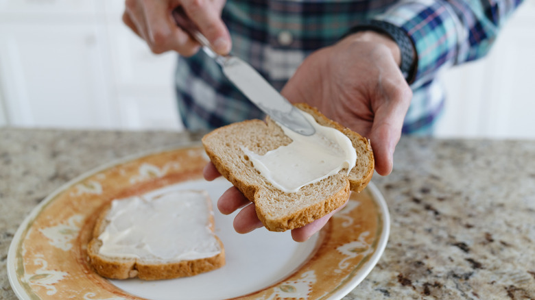 Person spreading mayonnaise on bread with knife.