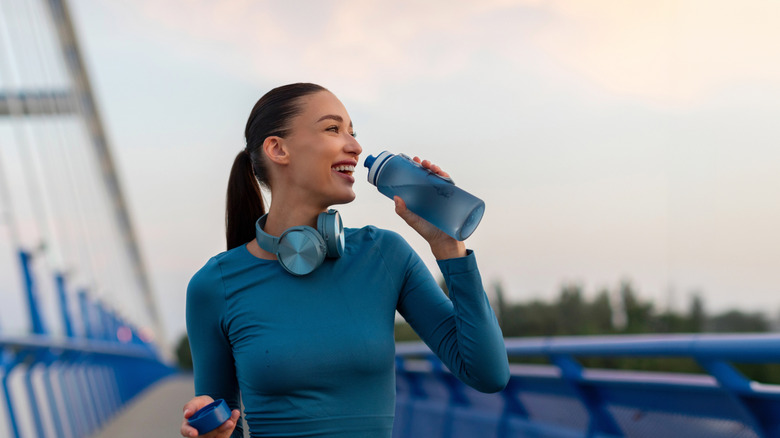 A woman drinks water on a bridge