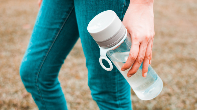 A hand carries a reusable plastic water bottle