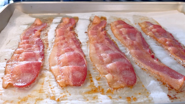 Five strips of sizzling bacon on parchment paper-lined baking sheet