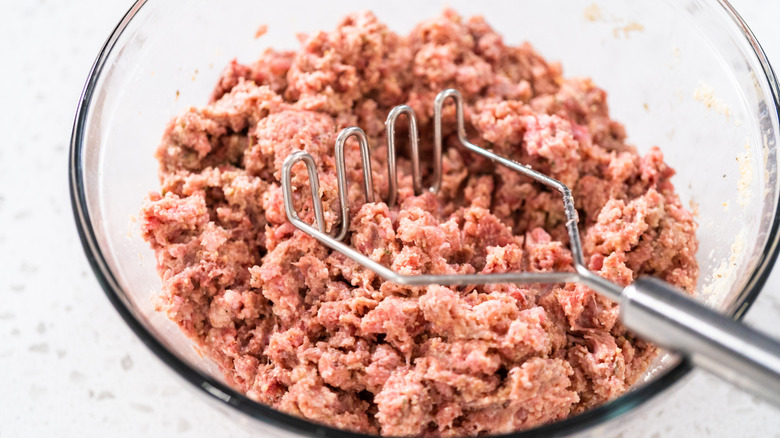 Mixing ingredients into meat with a potato masher.