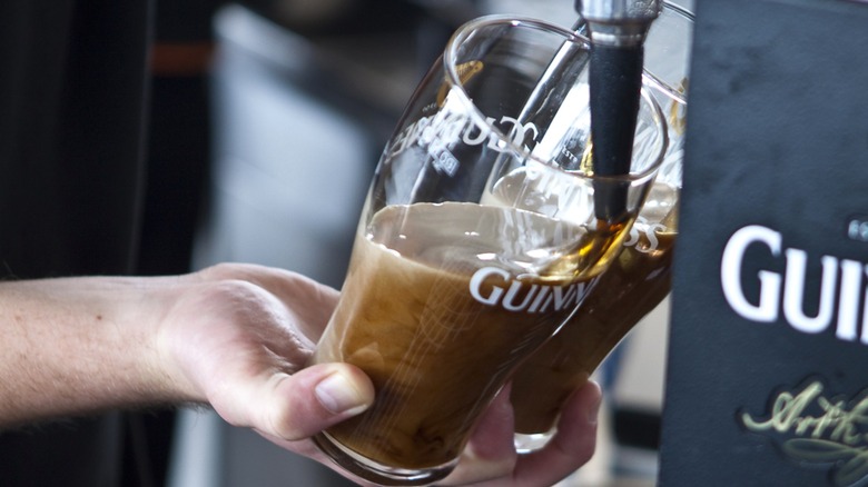 Person pouring Guinness into glasses from tap