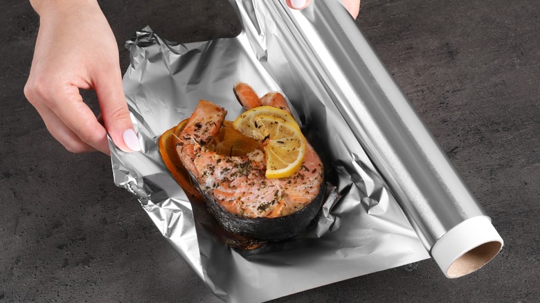 Person wrapping salmon with lemon slice on top in foil