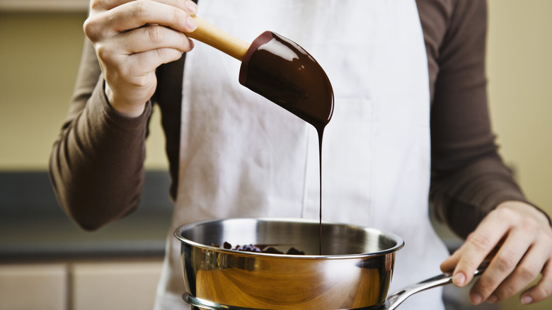 Man in an apron with glossy melted chocolate on a spatula