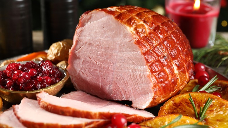 Ham with slices sliced off on table with cranberries and orange slices