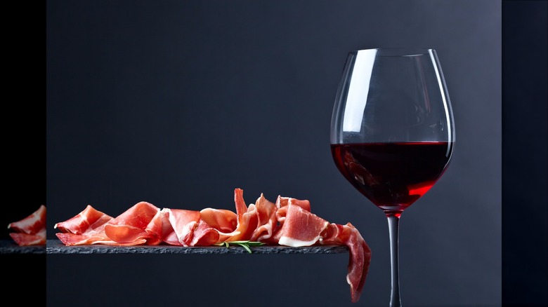 slate board with thinly sliced ham floating next to a glass of red wine
