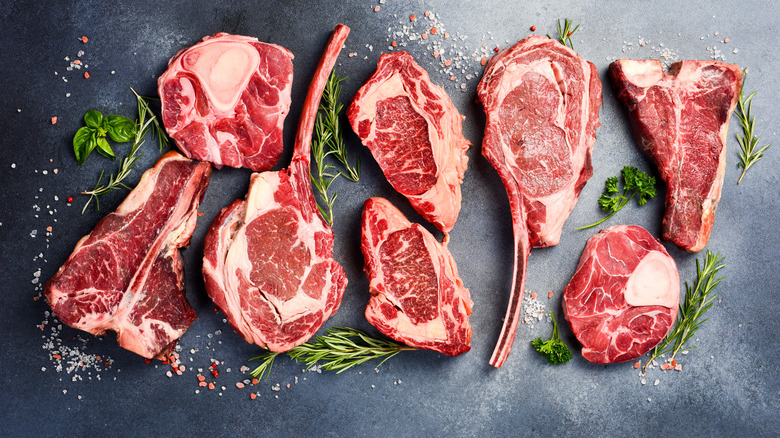 different cuts of raw steaks on a dark background with herbs and spices