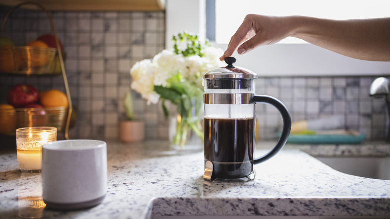 French press on countertop with hand depressing press plunger.