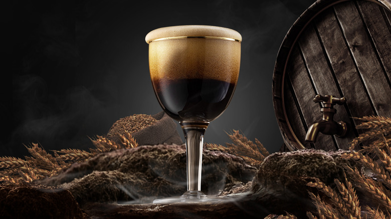 Stout beer in glass with barrel, grains, and dark background.