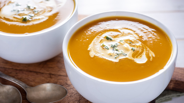 Two bowls of butternut squash soup topped with cream and herbs